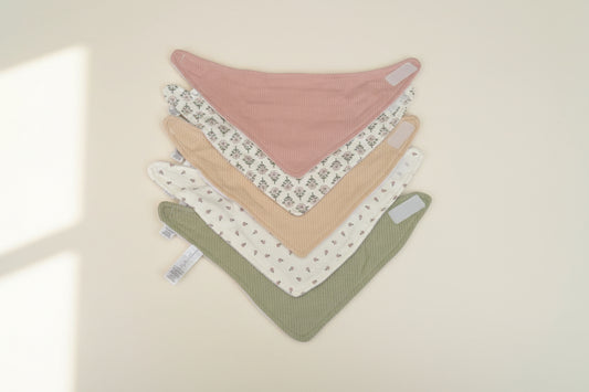 Set of 5 of colorful baby bibs on a warm white background.