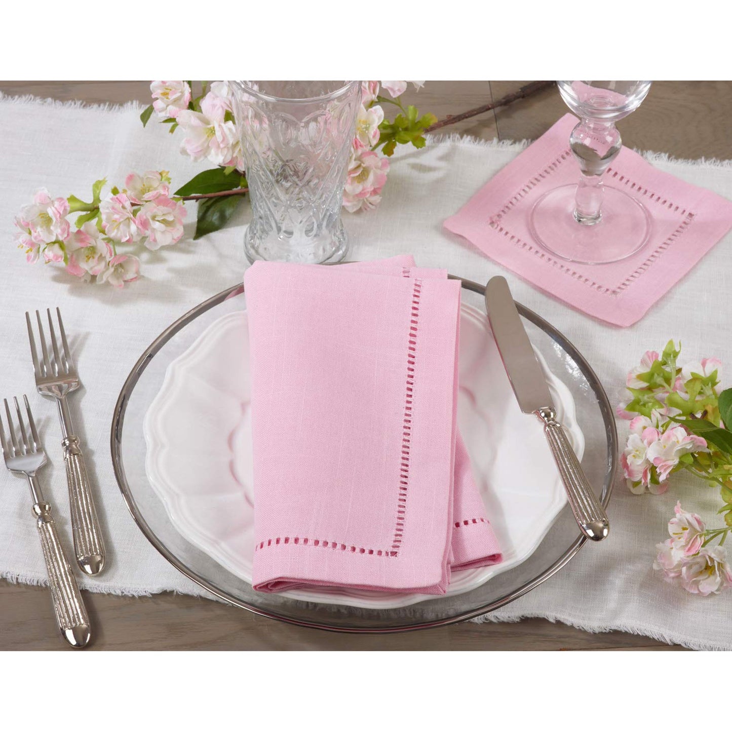 Table setting with pink napkins, silverware, and floral decorations on a white tablecloth.