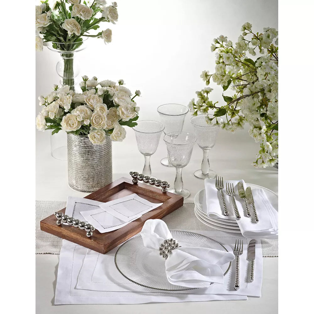 Elegant table setting with white flowers, silverware, and glassware on a white tablecloth.