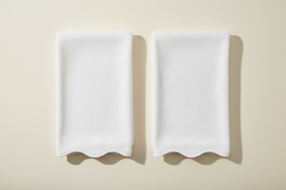 White scalloped-edge towels on a decorative fabric on a warm white background