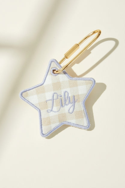 Star-shaped keychain with name embroidery on a beige surface