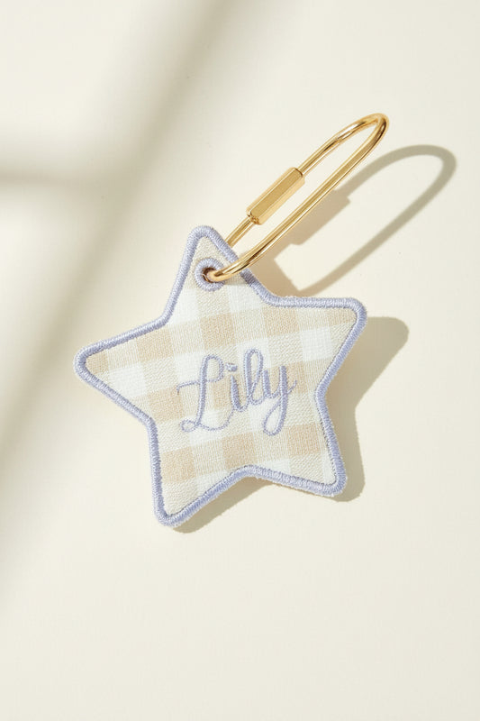Star-shaped keychain with name embroidery on a beige surface