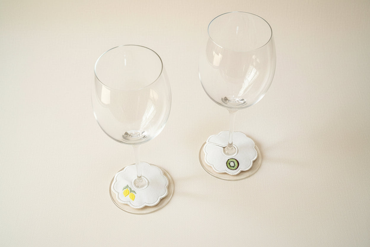 Two wine glasses with decorative embroidered stem tags on a beige surface