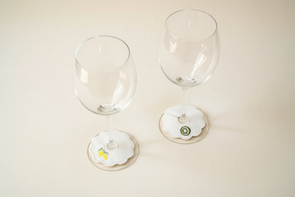 Two wine glasses with decorative embroidered stem tags on a beige surface