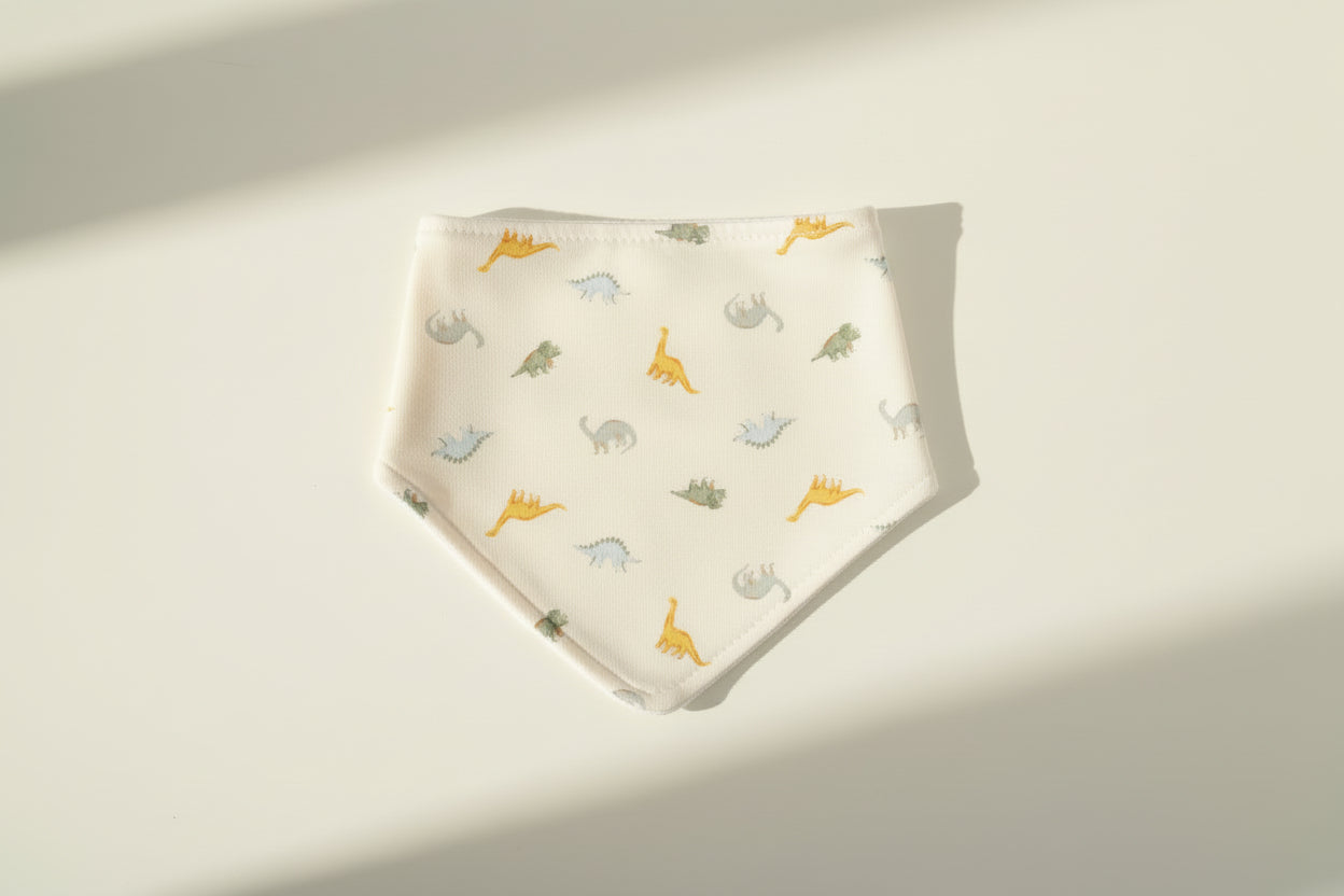 Baby bib with dinosaur pattern on a warm white background