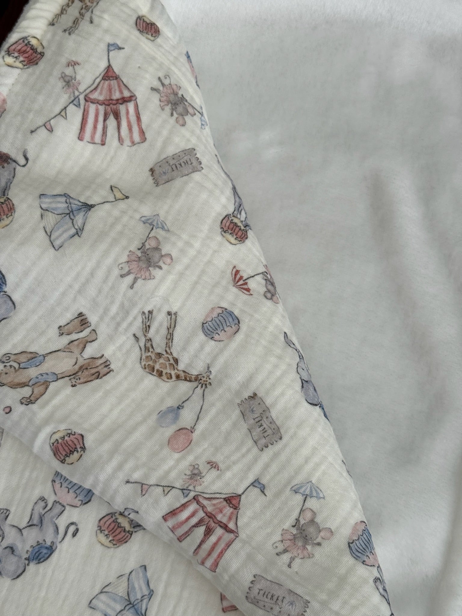 Baby blanket with colorful animal and circus tent patterns showing white polyester back