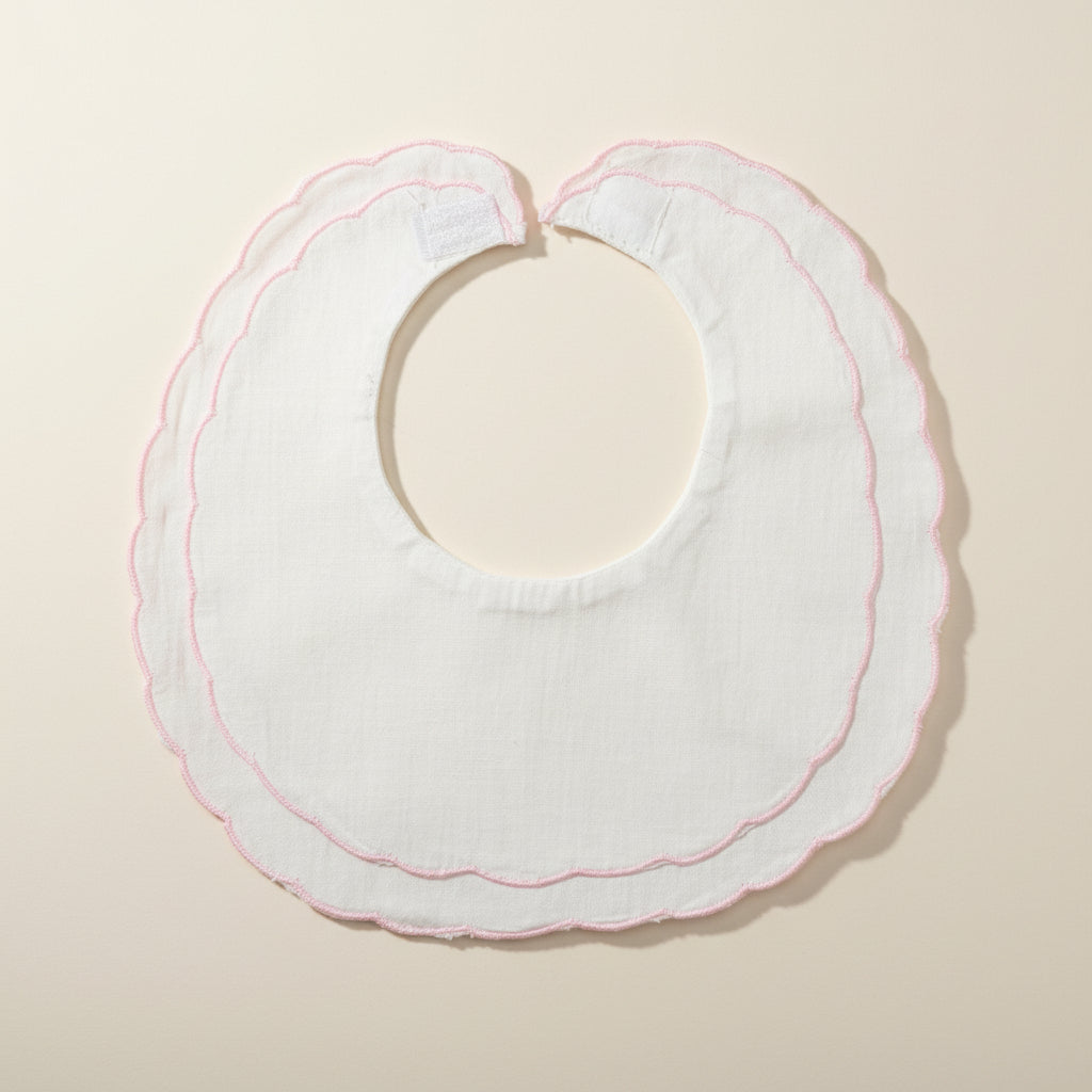 White baby bib with pink trim on a beige surface