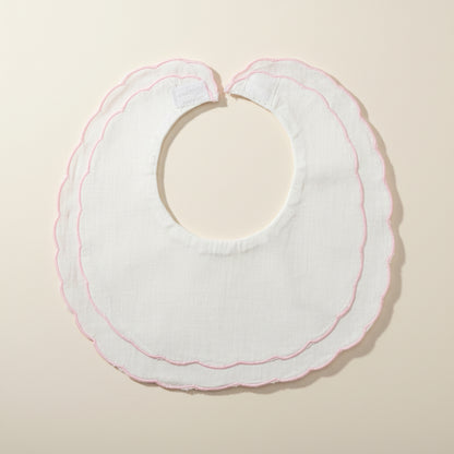 White baby bib with pink trim on a beige surface