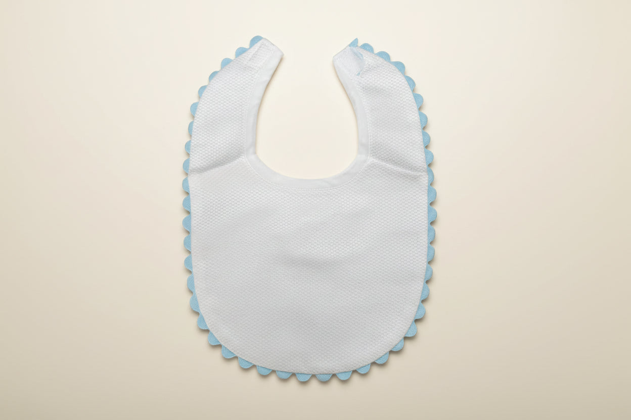 White baby bib with blue trim on a beige surface