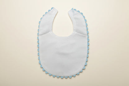 White baby bib with blue trim on a beige surface