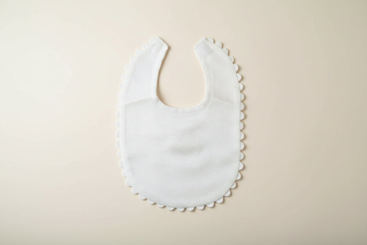 White baby bib with scalloped edge on a beige surface