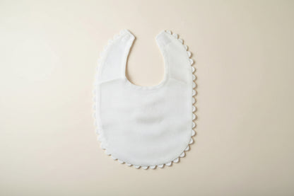 White baby bib with scalloped edge on a beige surface