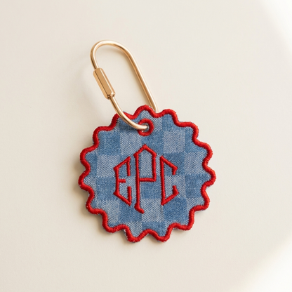 Fabric keychain with blue checkered design and red monogram on a beige background