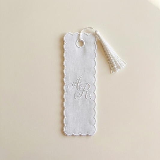 White scalloped bookmark with tassel on a beige background